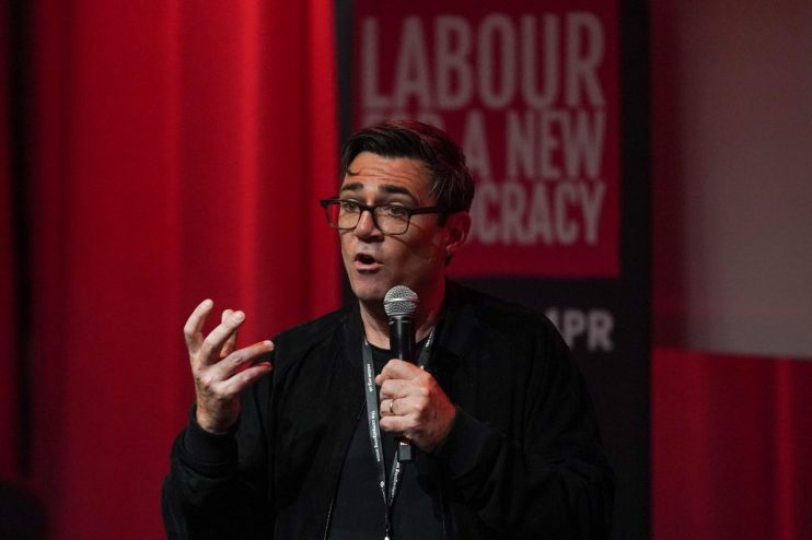 Andy Burnham speaking at a Labour Party event, addressing current political issues, with a focused and determined expression.