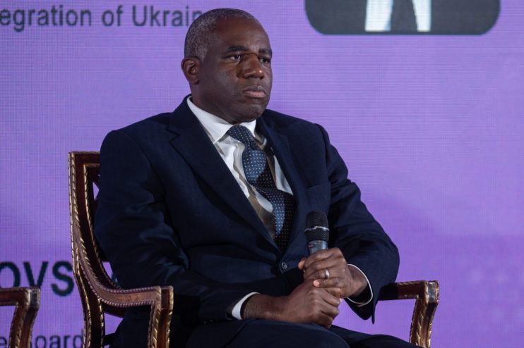 David Lammy speaking at a podium during a press conference, addressing current political issues, wearing a suit and tie.