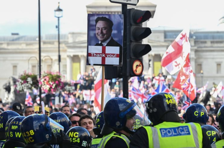Crowd of protesters holding signs and banners during a public demonstration in a city street, expressing civil unrest.