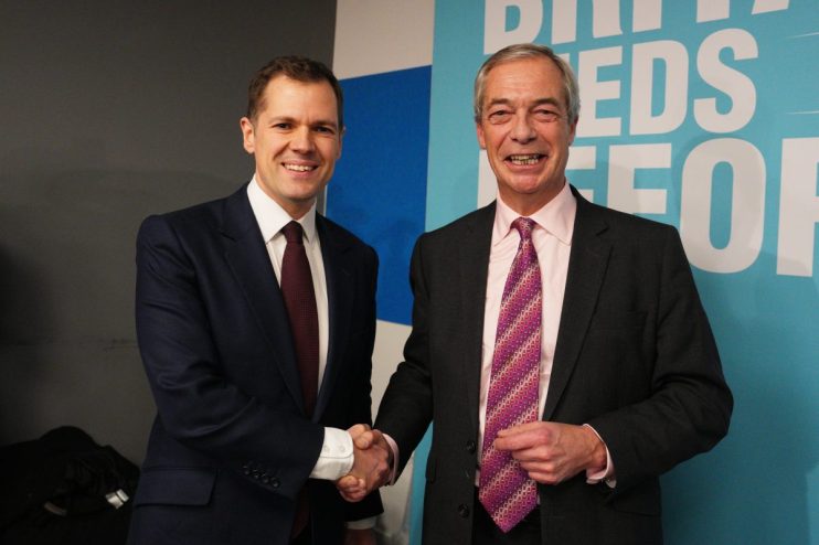 Robert Jenrick and Nigel Farage in discussion at a public event, showcasing political engagement and dialogue.