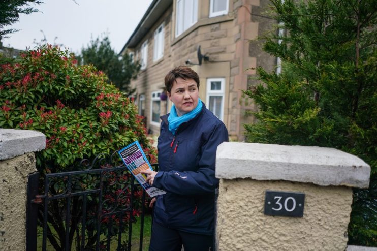 Ruth Davidson speaking at a public event, wearing a formal suit, addressing a large audience with a serious expression.