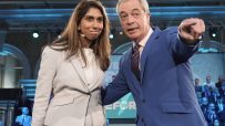 Suella Braverman and Nigel Farage in discussion at a political event, both dressed in formal attire, engaging in a serious...