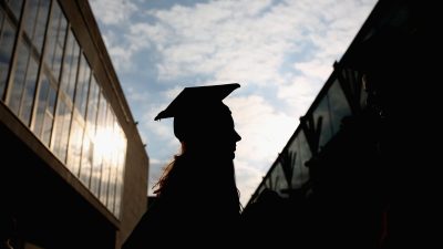 UK university graduate in cap and gown holding diploma at a campus ceremony, celebrating academic achievement and success