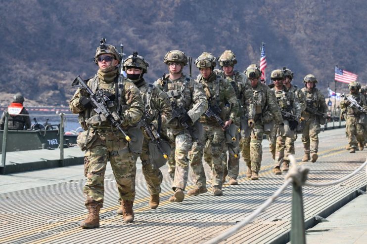 US Army personnel in uniform engaged in strategic planning session in a conference room with maps and digital displays vis...