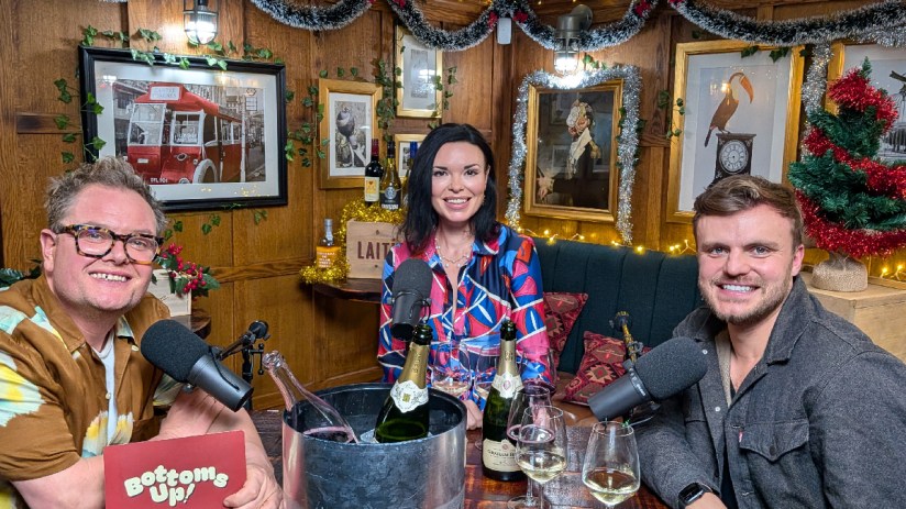 Alan Carr smiling onstage during a comedy show, wearing a colorful outfit, engaging audience with lively performance.