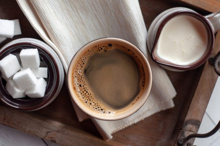 Freshly brewed coffee with a splash of milk and sugar cubes on a wooden table, highlighting morning beverage essentials