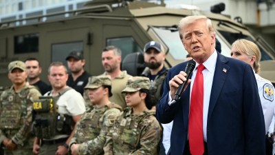 Donald Trump speaking at a press conference, addressing media questions, wearing a suit and tie, with American flags in ba...