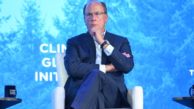 Larry Fink, CEO of BlackRock, speaking at a business conference, wearing a suit and glasses, gesturing with his hands