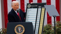 President Trump addressing the media during a press conference, wearing a navy suit and red tie, with the American flag in...