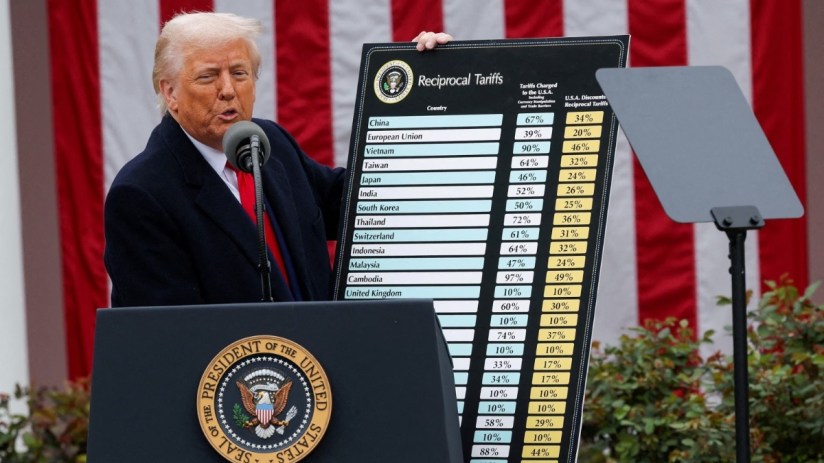 President Trump addressing the media during a press conference, wearing a navy suit and red tie, with the American flag in...