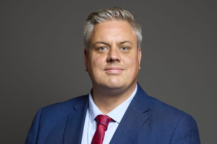 Blair McDougall discussing political strategies at a conference podium, emphasizing key points in front of an engaged audi...