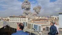 Iran explosion aftermath showing smoke billowing from a building, emergency response teams on site, and debris scattered a...