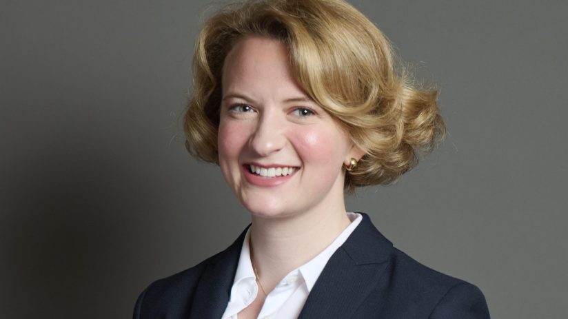 Katie Lam presenting at a business conference, standing confidently on stage with a projector screen displaying charts.