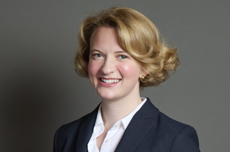 Katie Lam presenting at a business conference, standing confidently on stage with a projector screen displaying charts.