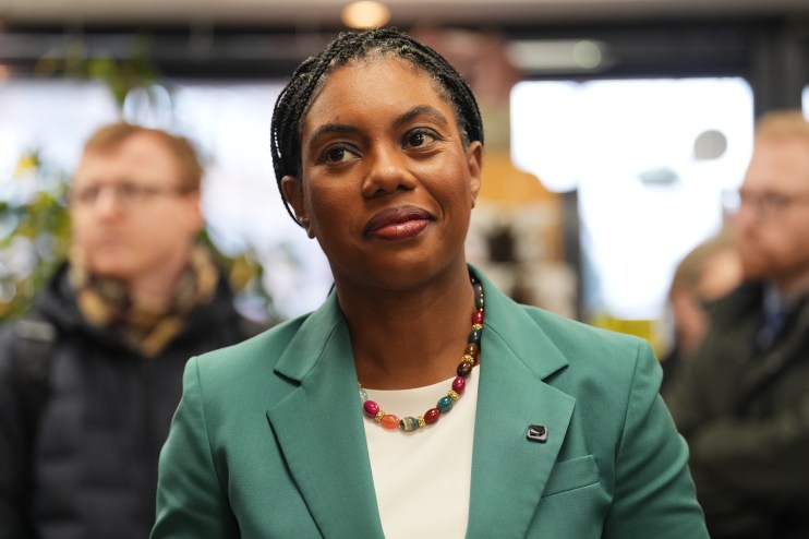 Kemi Badenoch speaking at a podium during a press conference, wearing a professional suit, addressing economic policies