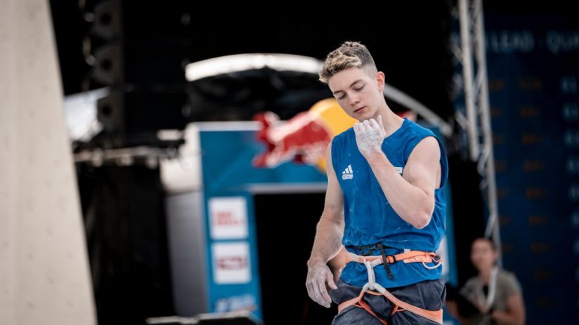 Breaking news event with a large crowd gathered in a city square, people holding signs, and a backdrop of modern buildings