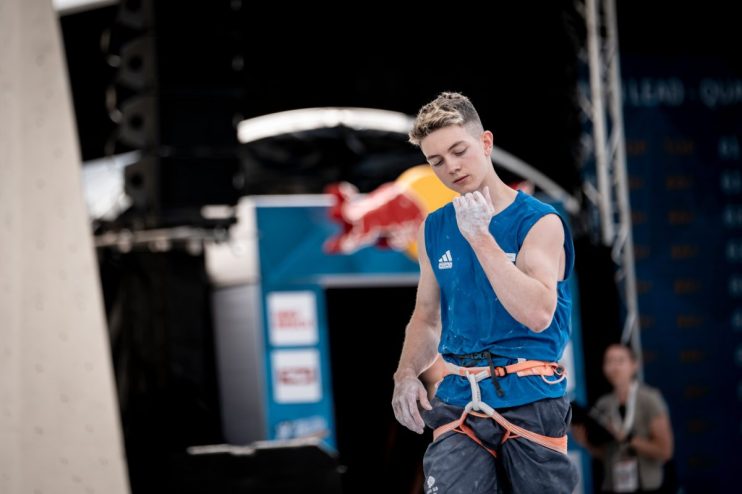 Breaking news event with a large crowd gathered in a city square, people holding signs, and a backdrop of modern buildings