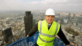 Gerald Ronson in a suit at a business conference, gesturing during a keynote speech, engaging with the audience.