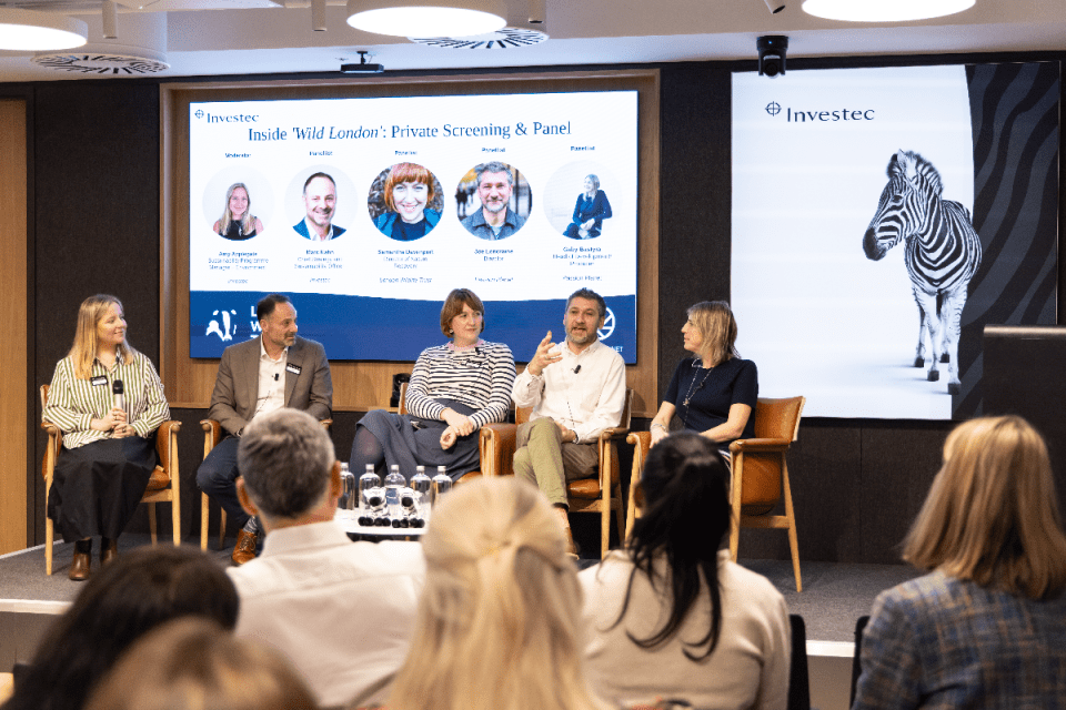 Breaking news event with diverse crowd gathered in city square, featuring banners and a stage setup for keynote speakers
