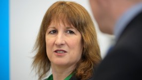 Rachel Reev addressing an audience at a business conference podium, wearing a blue blazer, discussing economic trends.