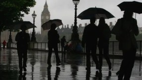 Rainy and gloomy British landscape with overcast skies, wet streets, and people holding umbrellas in a busy city setting.