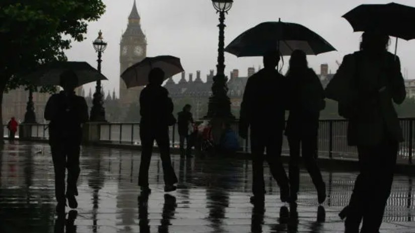Rainy and gloomy British landscape with overcast skies, wet streets, and people holding umbrellas in a busy city setting.