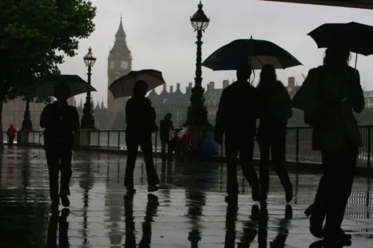 Rainy and gloomy British landscape with overcast skies, wet streets, and people holding umbrellas in a busy city setting.