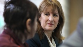 Keanu Reeves in a thoughtful pose, wearing a formal suit, looking contemplative during a business meeting or press event.
