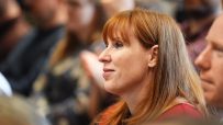 Angela Rayner speaking at a podium during a conference, addressing audience with a serious expression and gesturing with h...