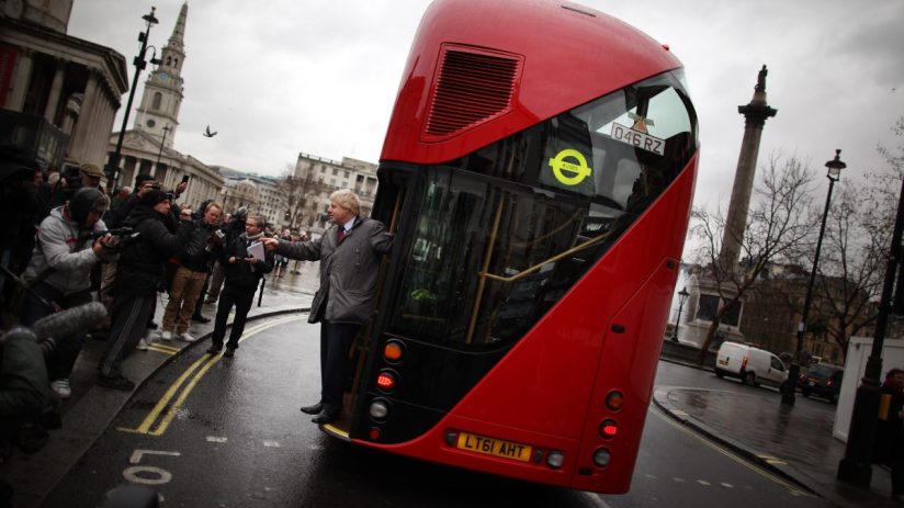 Boris Johnson standing beside a campaign bus with bold slogans, highlighting political messaging during election tour