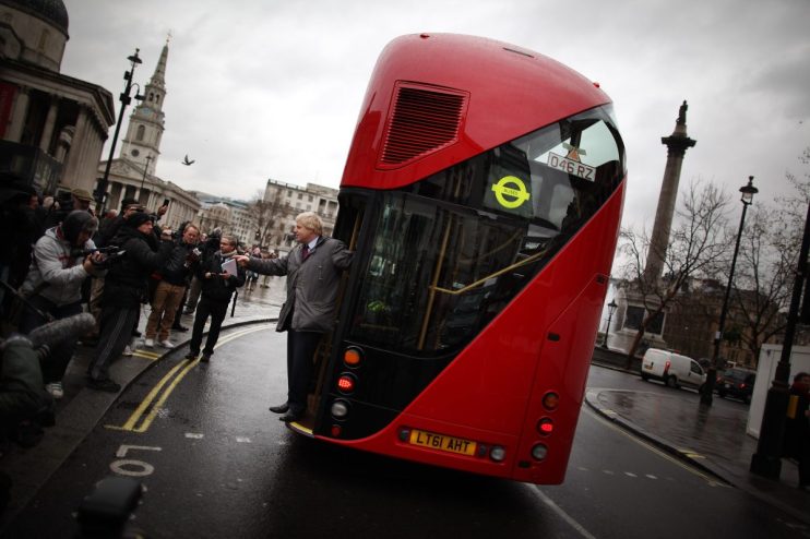 Boris Johnson standing beside a campaign bus with bold slogans, highlighting political messaging during election tour