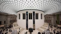 Exterior view of the British Museum with visitors walking along the entrance, showcasing its neoclassical architecture.