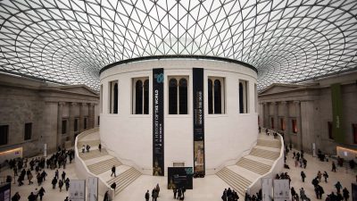 Exterior view of the British Museum with visitors walking along the entrance, showcasing its neoclassical architecture.