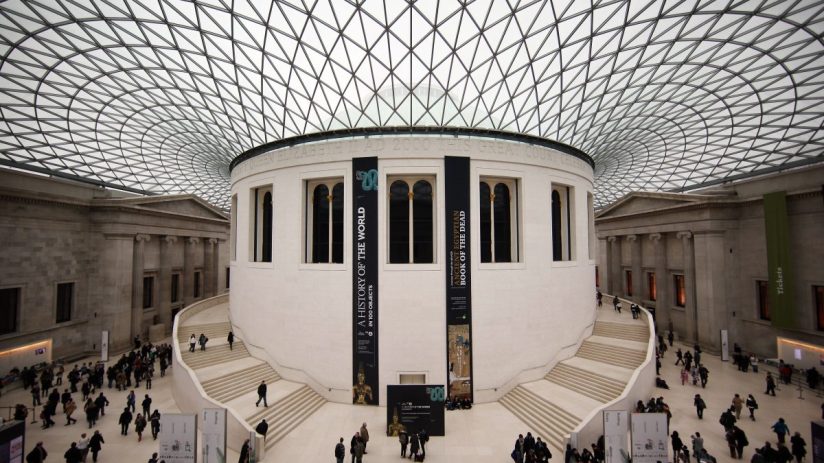 Exterior view of the British Museum with visitors walking along the entrance, showcasing its neoclassical architecture.