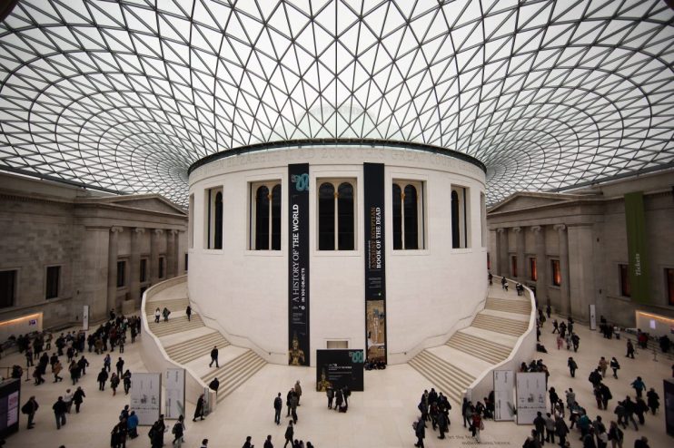 Exterior view of the British Museum with visitors walking along the entrance, showcasing its neoclassical architecture.