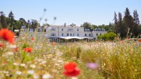 Coworth Parks Mansion House exterior amidst vibrant summer meadow, part of the Dorchester Collections luxury offerings.