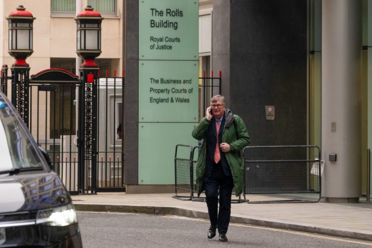 Crispin Odey attending a high-profile business event, wearing a formal suit, surrounded by investors and financial experts.
