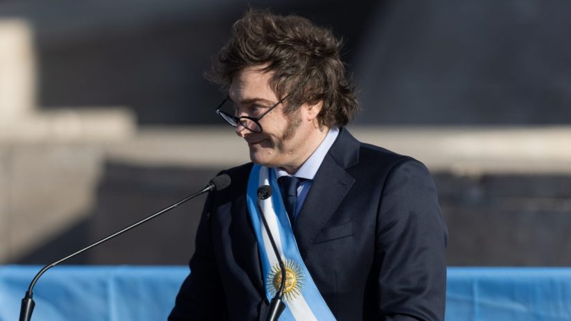 JavierMalei presents a keynote speech at a business conference, engaging with a diverse audience in a modern auditorium.