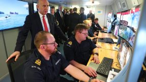 John Healey speaking at a podium, addressing an audience at a business conference, emphasizing economic strategies.