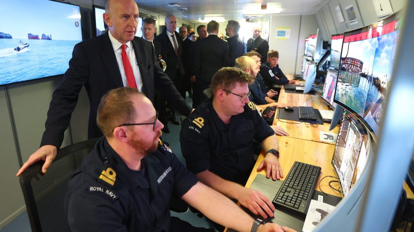 John Healey speaking at a podium, addressing an audience at a business conference, emphasizing economic strategies.