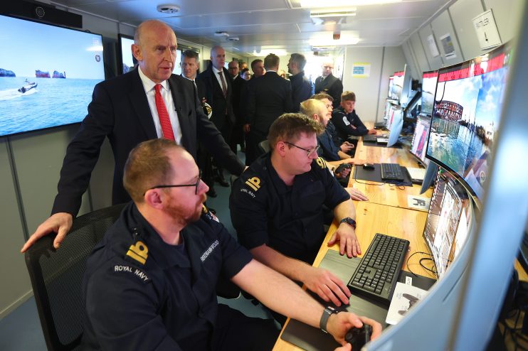 John Healey speaking at a podium, addressing an audience at a business conference, emphasizing economic strategies.