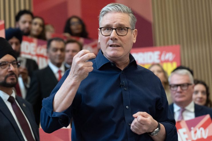 Keir Starmer speaking passionately at a Labour Party rally with supporters and banners in the background