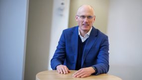 Richard Moriarty speaking at a business conference podium with audience in background, discussing industry insights