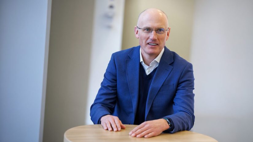 Richard Moriarty speaking at a business conference podium with audience in background, discussing industry insights