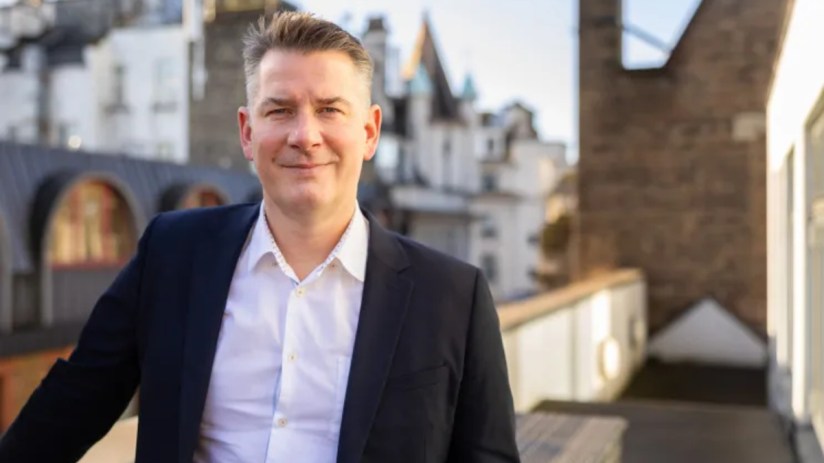 Stuart Neal, CEO of Boku, standing in an office wearing a suit, representing leadership in mobile payment solutions.