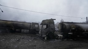 Charred oil tankers aftermath of an explosion at a refinery, with smoke billowing and emergency crews assessing the damage.