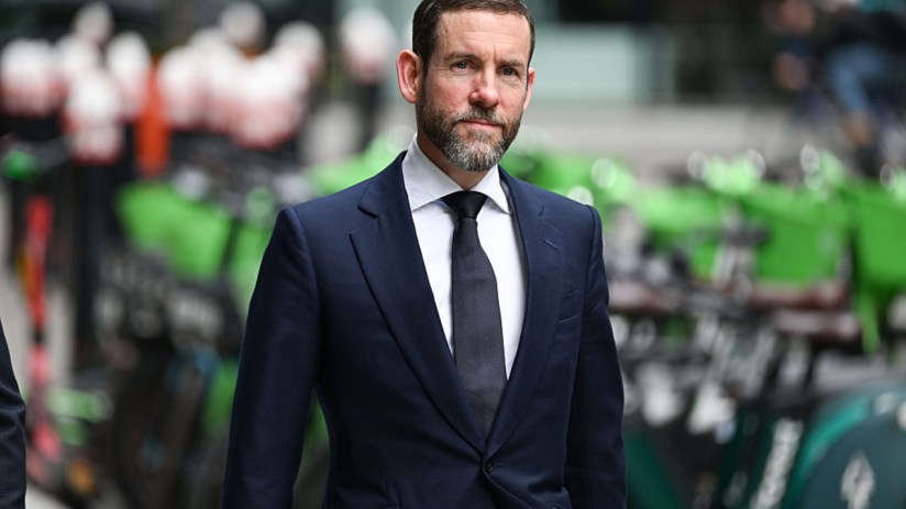 Lex Greensill speaking at a business conference, wearing a suit and tie, gesturing with his hand while discussing financia...