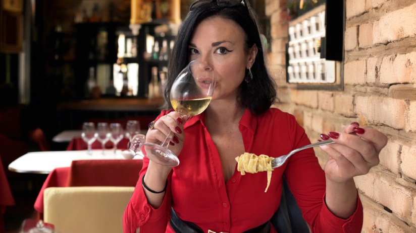 Libby enjoying a glass of authentic Italian wine at a vineyard, surrounded by lush grapevines and a scenic landscape.