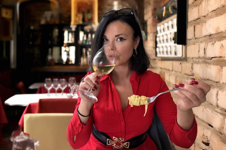 Libby enjoying a glass of authentic Italian wine at a vineyard, surrounded by lush grapevines and a scenic landscape.
