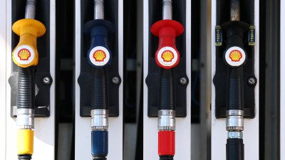 Petrol station with fuel pumps, signage displaying fuel prices, vehicles refueling, and customers engaging with attendants
